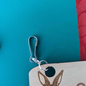 May include: A wooden keyring with a laser-engraved design of a rabbit's head. The keyring has a silver metal loop and a silver metal clasp.