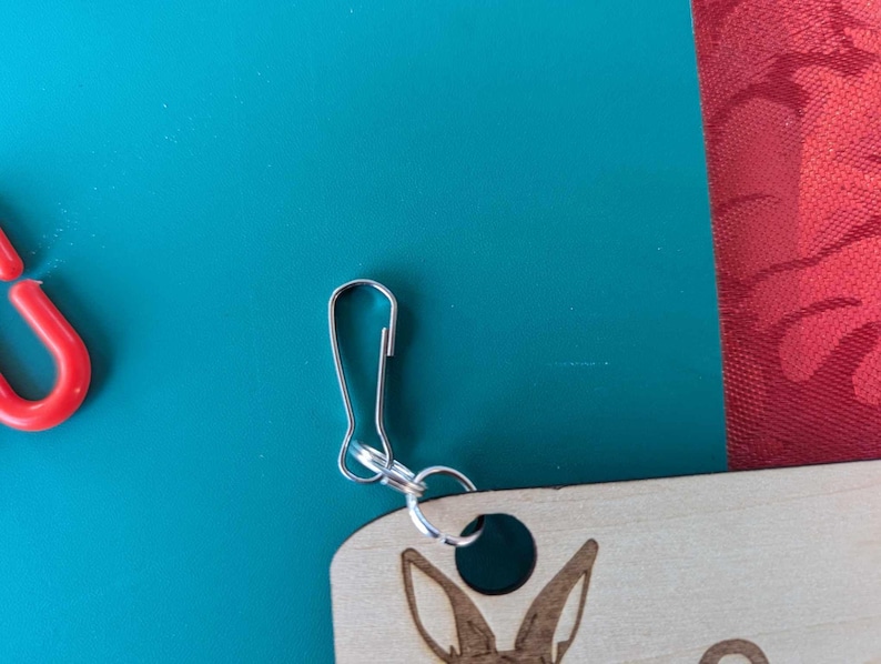 May include: A wooden keyring with a laser-engraved design of a rabbit's head. The keyring has a silver metal loop and a silver metal clasp.
