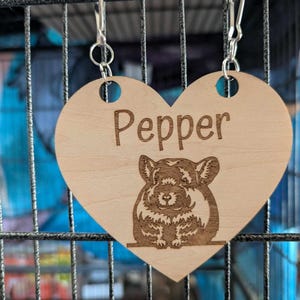 May include: A wooden heart-shaped pet tag with a chinchilla illustration and the name "Pepper" engraved on it. The tag is attached to a silver chain.