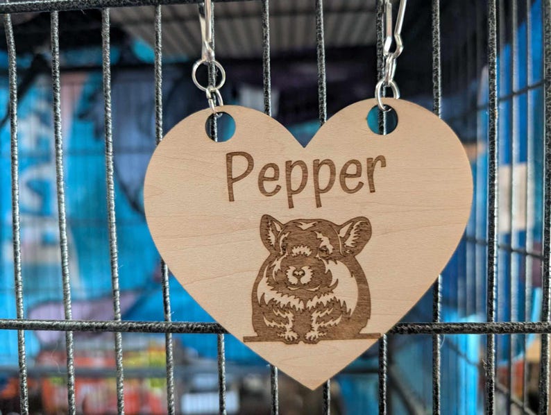 May include: A wooden heart-shaped pet tag with a chinchilla illustration and the name "Pepper" engraved on it. The tag is attached to a silver chain.