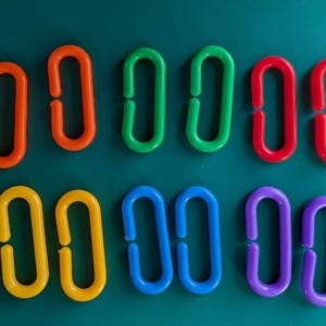 May include: A set of 10 colourful plastic rings, each with a different colour: red, orange, yellow, green, blue, purple, and two shades of blue. The rings are all the same size and shape, and they are arranged in a row.