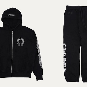 May include: A black zip-up hoodie and matching sweatpants set. The hoodie features a white circular logo on the chest, white text on the hood, and white graphic patterns on the sleeves. The sweatpants have a white circular logo and white text.