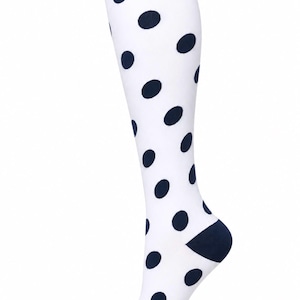 May include: A knee-high sock featuring a white base with a repeating pattern of dark navy blue polka dots. The sock includes a solid dark navy blue ribbed cuff at the top, a dark navy blue heel section, and a dark navy blue toe cap.