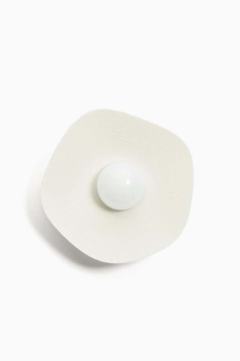 May include: A white ceramic wall sconce with a round, white light bulb in the center.