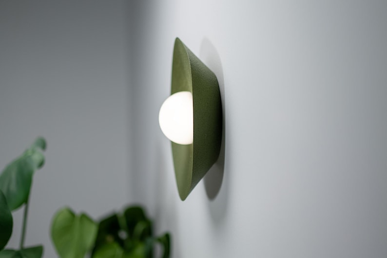 May include: A green wall sconce with a white light bulb. The sconce is made of a textured material and has a curved shape.