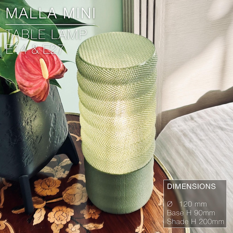 May include: A green table lamp with a woven shade and a cylindrical base. The lamp is 120 mm in diameter, 90 mm tall at the base, and 200 mm tall at the shade. The lamp is labeled "MALLA MINI TABLE LAMP E14 & E27".