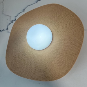 May include: A round, white light fixture with a woven, beige, circular shade.