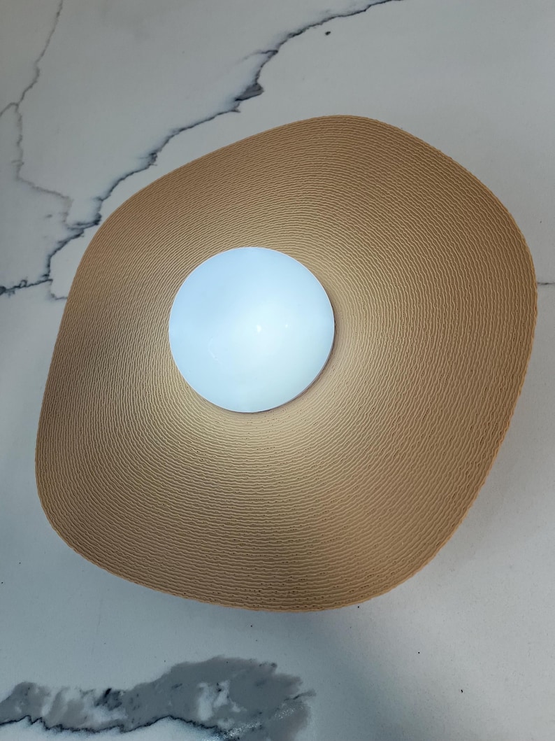 May include: A round, white light fixture with a woven, beige, circular shade.