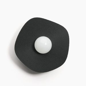 May include: A black, round, wall-mounted light fixture with a white, round light bulb in the center.