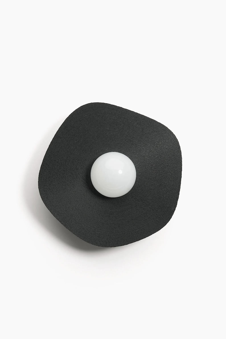 May include: A black, round, wall-mounted light fixture with a white, round light bulb in the center.
