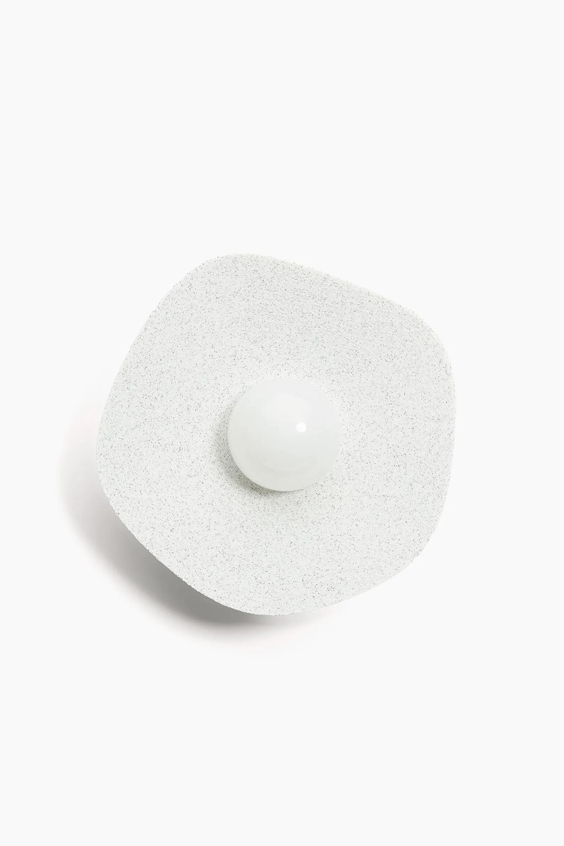 May include: A white, round, speckled, wall-mounted light fixture with a white, round, frosted glass shade.