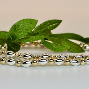 May include: Two bracelets made of oval-shaped beads. One bracelet is made of gold beads and the other is made of silver beads.