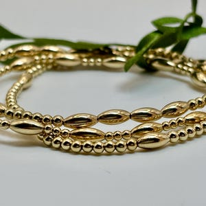 May include: Three gold bracelets with round and oval beads. The bracelets are stacked on top of each other.