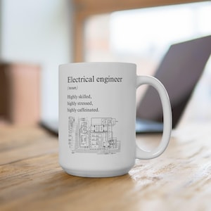Könnte beinhalten: Eine weiße Keramiktasse mit einem schwarz-weißen Design. Die Tasse zeigt die Definition eines Elektroingenieurs: "Hochqualifiziert, hochgestresst, hochkoffeiniert."