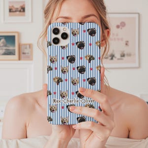 Puede incluir: Una funda de tel&eacute;fono a rayas azules y blancas con un patr&oacute;n repetido de caras de gatos y perros, y huellas de patas rojas. La funda tiene los nombres "Max-Charlie-Oliver" impresos.