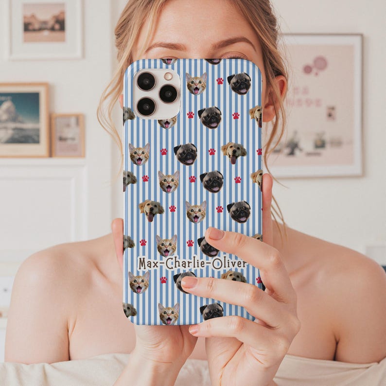 Puede incluir: Una funda de tel&eacute;fono a rayas azules y blancas con un patr&oacute;n repetido de caras de gatos y perros, y huellas de patas rojas. La funda tiene los nombres "Max-Charlie-Oliver" impresos.