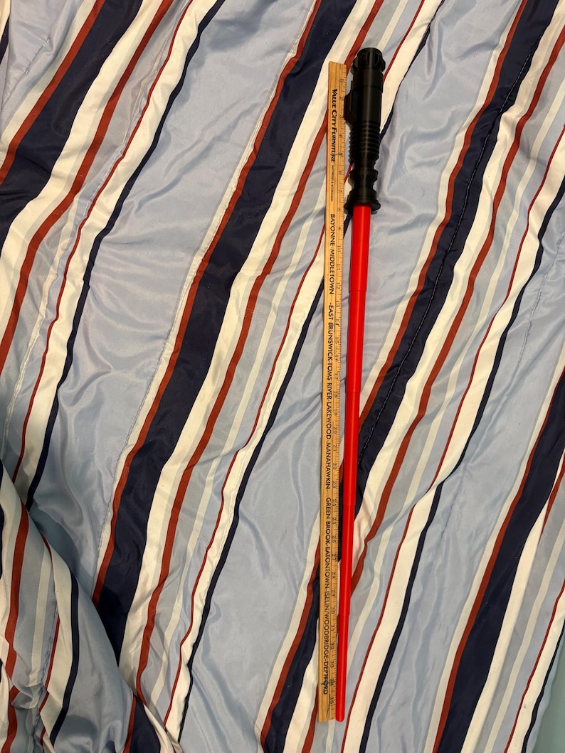 May include: A red and black lightsaber toy with a black handle and a red blade. The blade is about 30 inches long.