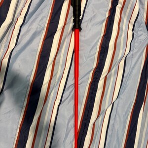 May include: A red lightsaber toy with a black handle. The lightsaber is lying on a blue and white striped fabric.