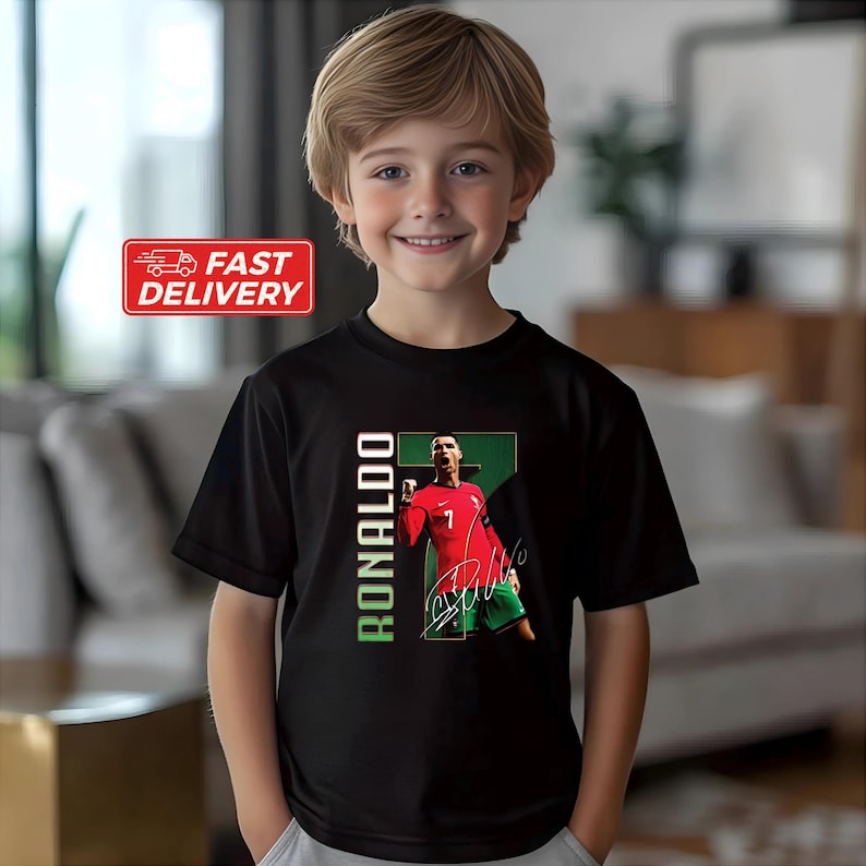 Puede incluir: Una camiseta negra con un gr&aacute;fico de un jugador de f&uacute;tbol con una camiseta roja con el n&uacute;mero 7. El nombre del jugador, "RONALDO", est&aacute; impreso verticalmente en verde. La camiseta la lleva una persona joven.