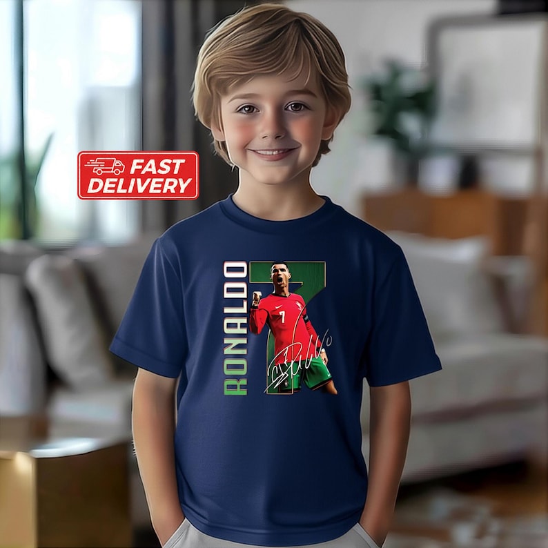 Puede incluir: Camiseta azul marino con un gr&aacute;fico de un jugador de f&uacute;tbol con una camiseta roja. El n&uacute;mero 7 es visible. La palabra "RONALDO" est&aacute; impresa verticalmente en verde y blanco. La camiseta la lleva una persona joven.