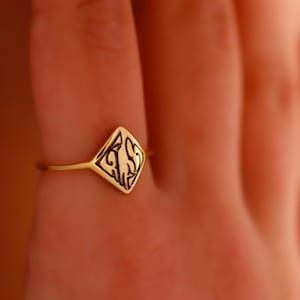 May include: A gold ring with a diamond-shaped design featuring a black intricate pattern.