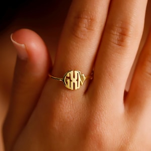 May include: A gold ring with a monogrammed circle featuring the letters "GXN".