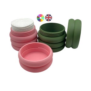 Op de afbeelding: Drie containers in roze en groen. Eén roze container is gevuld met watjes. De andere twee containers zijn leeg. De containers zijn gemaakt van een zacht, flexibel materiaal. De containers zijn ontworpen voor het opbergen van kleine items.