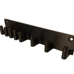 K&ouml;nnte beinhalten: Ein schwarzer, an der Wand montierter Schl&uuml;sselhalter mit acht gleichm&auml;&szlig;ig verteilten Haken. Die rechteckige R&uuml;ckplatte hat abgerundete Ecken und zwei L&ouml;cher zur Montage. Die Haken sind zylindrisch und ragen heraus. Der Schl&uuml;sselhalter besteht aus mattem, schwarzem Material.