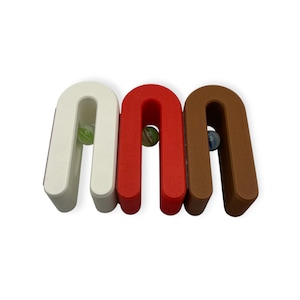 May include: Three U-shaped stands in white, red, and brown, each featuring a textured base and a smooth top arch. A single small glass marble is positioned within the open centre of each stand, showcasing green, white, and blue swirl patterns.