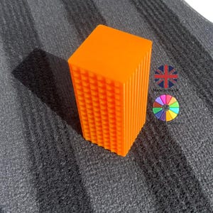 Puede incluir: Un bloque naranja brillante con una superficie texturizada. El bloque está hecho de plástico y tiene una forma cuadrada.