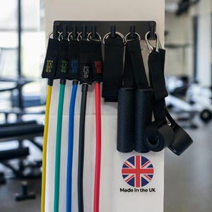 May include: A set of resistance bands with black handles and various colored tubes, including yellow, green, blue, black, and red. The bands are labeled with weight measurements in pounds and kilograms. The set is mounted on a black holder.