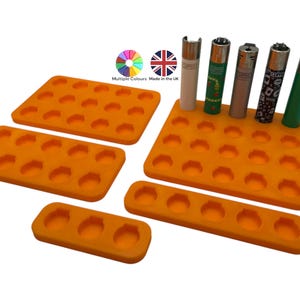 Puede incluir: Bandeja de almacenamiento de mecheros de silicona naranja con 24 ranuras individuales para mecheros. La bandeja está hecha en el Reino Unido y está disponible en varios colores. La imagen muestra cinco mecheros, cada uno con un diseño diferente.