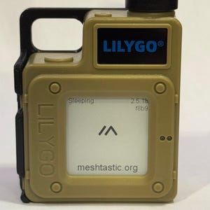 May include: A tan-colored LILYGO device with a black handle and antenna. The screen displays "Sleeping", a symbol, and "meshtastic.org". The LILYGO logo is in blue. The device has a rectangular shape with rounded corners and visible screws.