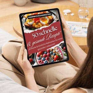 Könnte beinhalten: Ein digitales Tablet zeigt eine rote und weiße Grafik mit dem Text "50 schnelle & gesunde Rezepte" und dem Slogan "Einfache & köstliche Mahlzeiten für einen gesunden Lebensstil". Das Tablet wird von einer Person gehalten.