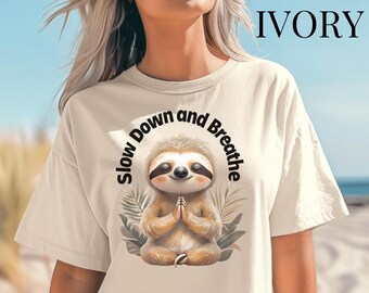 May include: A beige t-shirt with a graphic of a meditating sloth and the text "Slow Down and Breathe".