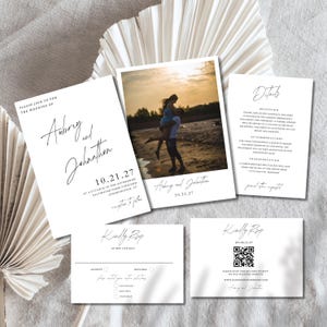 Puede incluir: Un conjunto de tarjetas de invitación de boda blancas con texto negro. Las tarjetas incluyen detalles sobre la boda, información de RSVP y una foto de una pareja. Las invitaciones presentan fuentes elegantes y un diseño minimalista.