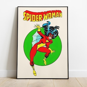Op de afbeelding: Een ingelijste poster met Spider-Woman in een dynamische pose. Het kunstwerk toont Spider-Woman in een rood en geel kostuum, tegen een groene cirkel. De woorden "SPIDER-WOMAN" worden weergegeven in gele en rode letters.