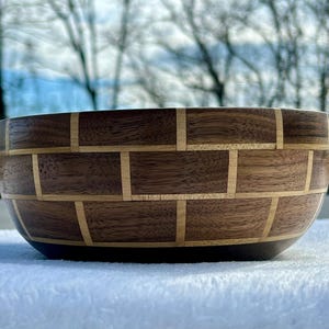 May include: A wooden bowl with a brick pattern made from walnut and maple wood. The bowl is round and has a dark brown color.