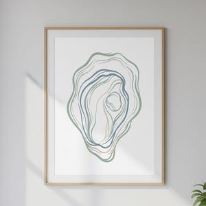 Peut inclure: Impression d'art abstrait dans un cadre en bois. L'œuvre présente un motif organique en couches dans des tons de bleu, de vert et de beige sur fond blanc. L'art encadré est exposé sur un bureau blanc, avec une petite plante en pot à proximité.