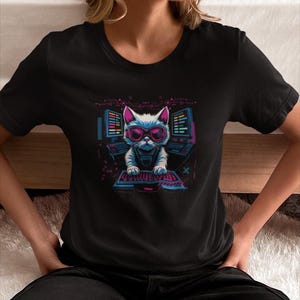 Op de afbeelding: Zwart t-shirt met een afbeelding van een witte kat met een roze zonnebril en een futuristische outfit, zittend voor computerschermen en een toetsenbord. De kattenafbeelding heeft een neon kleurenschema met roze, blauwe en paarse accenten. Het ontwerp is een speelse kijk op technologie.