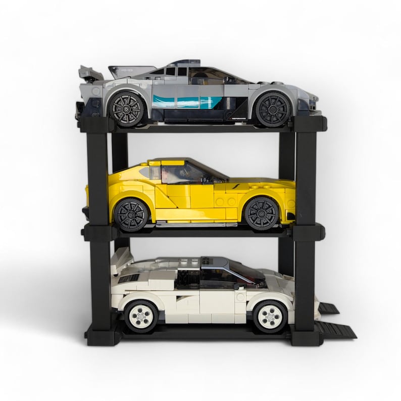 Puede incluir: Un expositor de coches de metal negro de tres niveles con tres coches de juguete. El coche de arriba es gris, el del medio es amarillo y el de abajo es blanco.