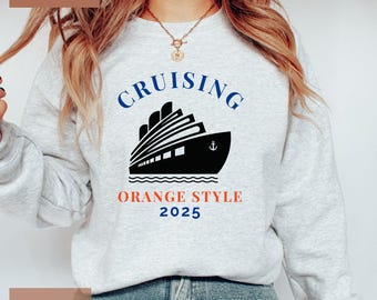 May include: Light gray sweatshirt with the word "CRUISING" in blue above a black and white graphic of a cruise ship. Below the ship is the text "ORANGE STYLE 2025" in red and blue.