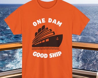 May include: Orange t-shirt with a graphic of a cruise ship and the words "ONE DAM GOOD SHIP" in white. The ship is black with white accents and an anchor. The shirt is displayed against a backdrop of the ocean.