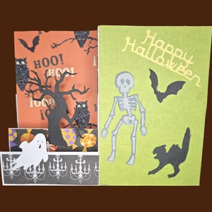 May include: Halloween-themed greeting cards with pop-up elements. One card features a tree, owls, and the word "Hoo!" on an orange background. The other card has a skeleton, bat, cat, and the words "Happy Halloween" on a green background.