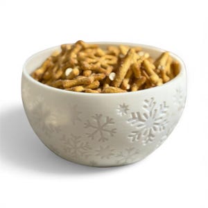 Puede incluir: Un cuenco de cerámica blanco lleno de una mezcla de aperitivos. El cuenco tiene un diseño de copo de nieve en relieve en el exterior. La mezcla de aperitivos es de color marrón dorado y contiene pretzels y otros ingredientes crujientes.