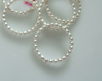May include: A collection of silver rings, each featuring a beaded design, are displayed. The rings are circular, with small, evenly spaced beads forming the ring's circumference. The rings are reflective, catching the light, and are on a white surface.