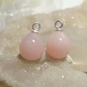 May include: Two pink opal teardrop charms with silver jump rings. The charms are about 1 inch long and 1/2 inch wide.