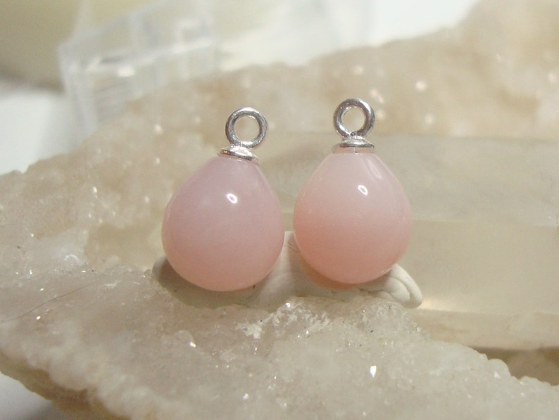May include: Two pink opal teardrop charms with silver jump rings. The charms are about 1 inch long and 1/2 inch wide.