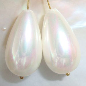 Peut inclure: Deux perles de forme larme de couleur blanc nacré avec une boucle de fil d'or en haut.