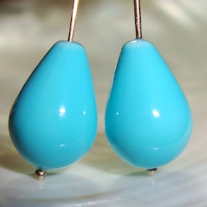 May include: A pair of teardrop-shaped earrings with a turquoise blue finish. The earrings are suspended from silver posts.